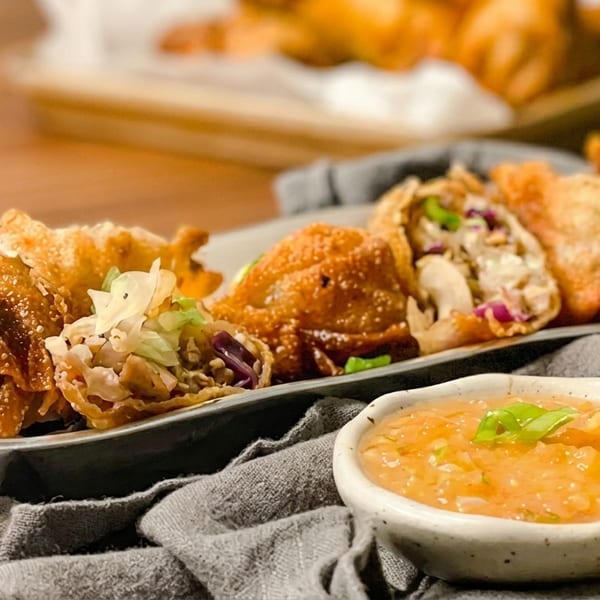 Crispy fried egg rolls and wontons with a side of sweet and sour sauce on a wooden table.